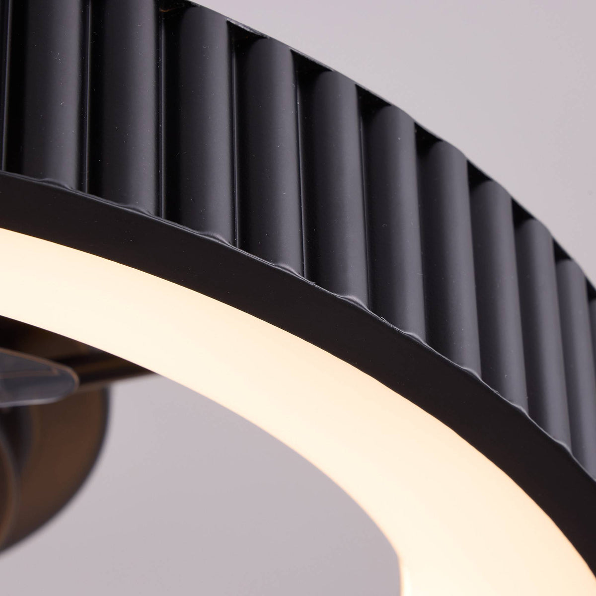 Close-up of 20" smart ceiling fan detail — black matte ribbed/fluted outer frame, warm white LED light ring, modern minimalist enclosure, premium texture