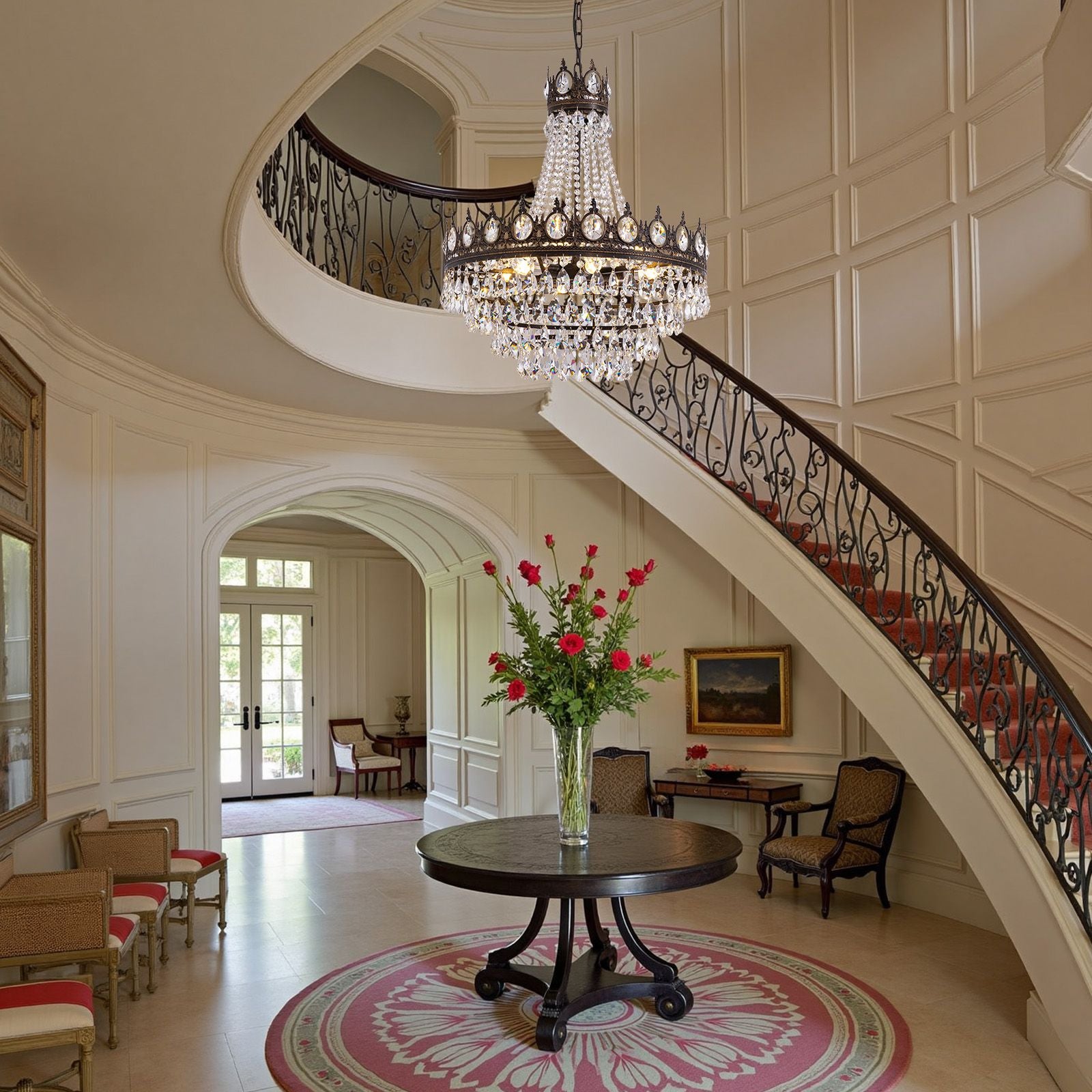 Aerian K9 Crystal Chandelier in grand staircase foyer — sweeping curved stairs, wrought iron railing, round table with red florals, dramatic entry statement | Sofary Lighting