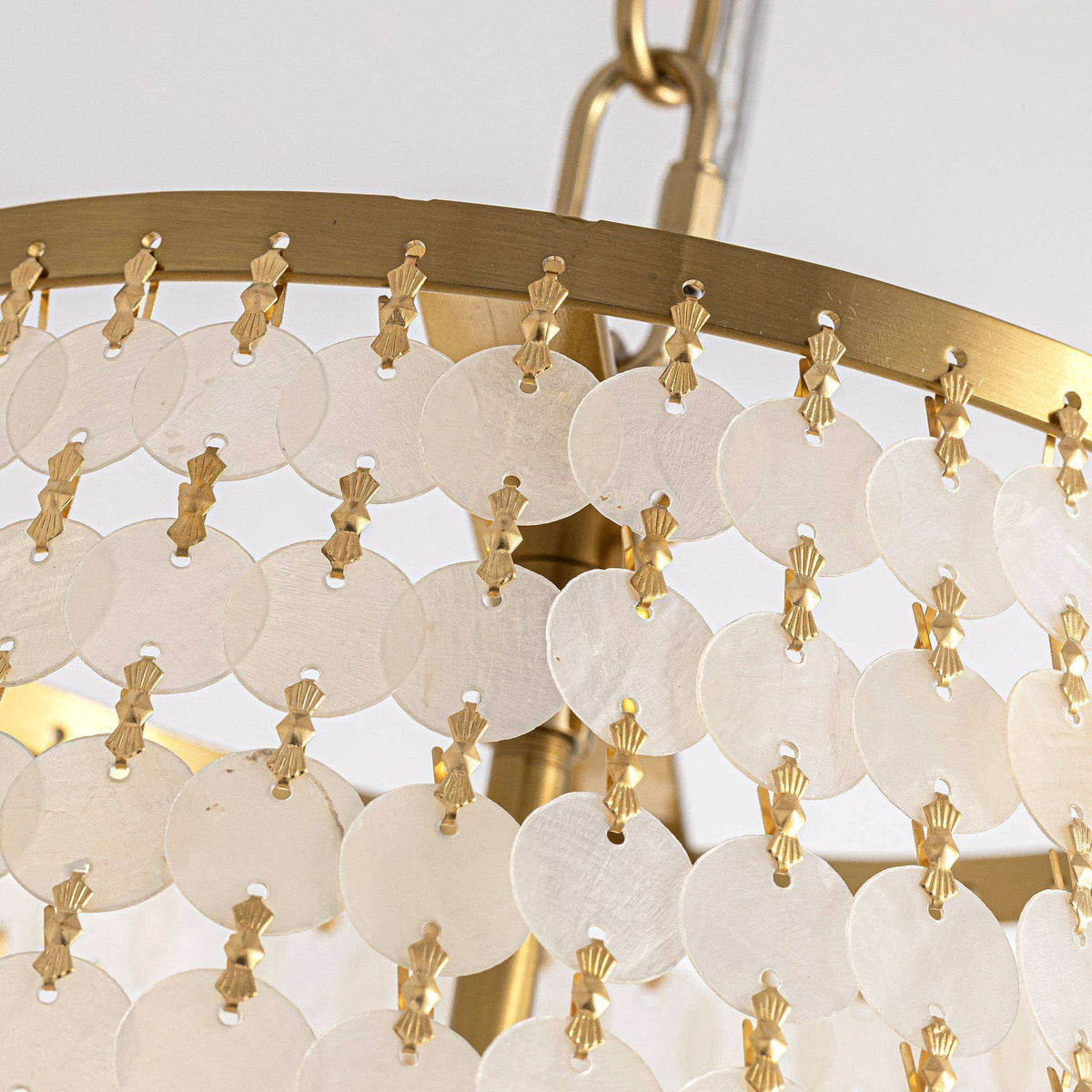 Close-up of Aeroh Shell Chandelier — gold metal ring, white circular shell/pearl discs strung with gold connectors, warm light diffusion, premium coastal craftsmanship | Sofary Lighting