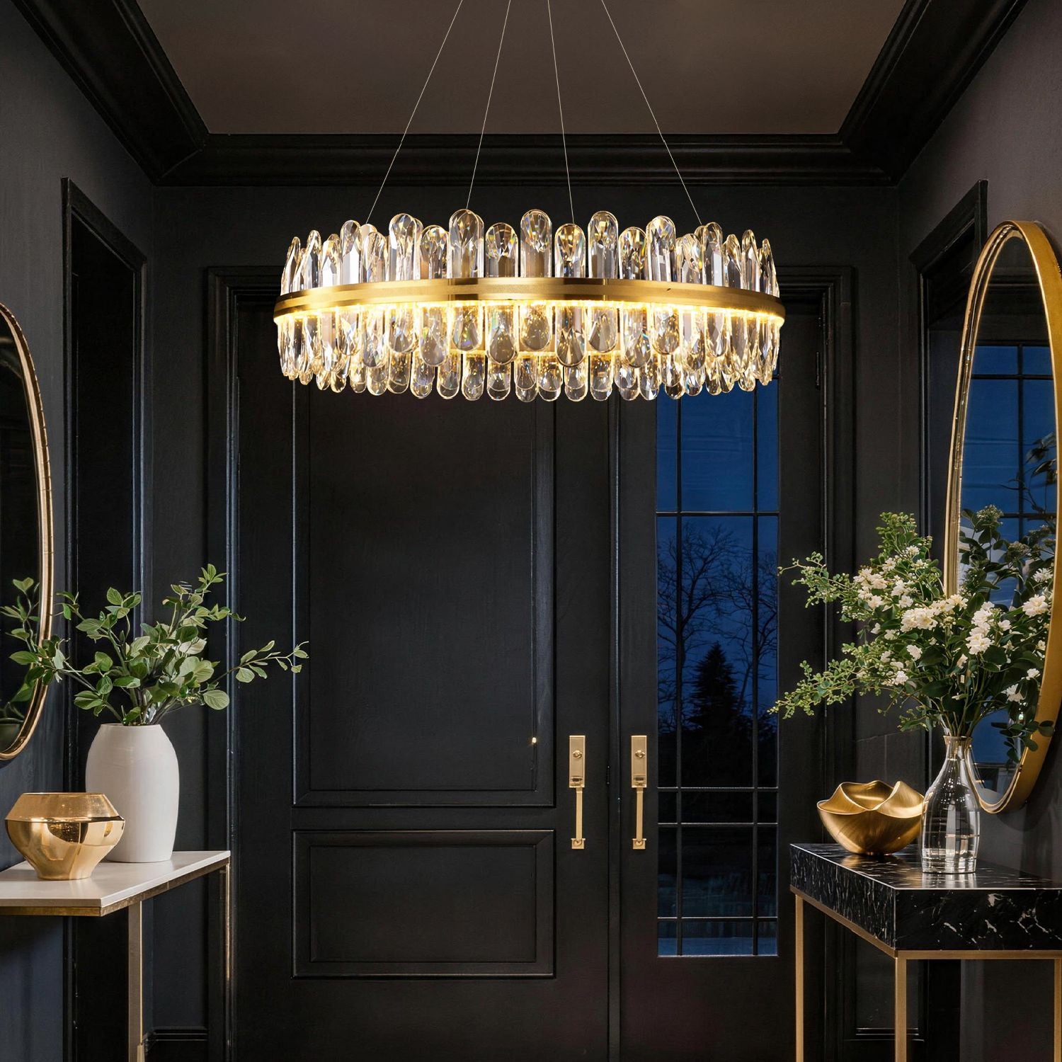 Aurelia Modern Luxury Champagne Gold K9 Crystal Chandelier in a foyer — hanging above double black doors with gold handles, dark paneled walls, and mirrored side tables | Sofary Lighting