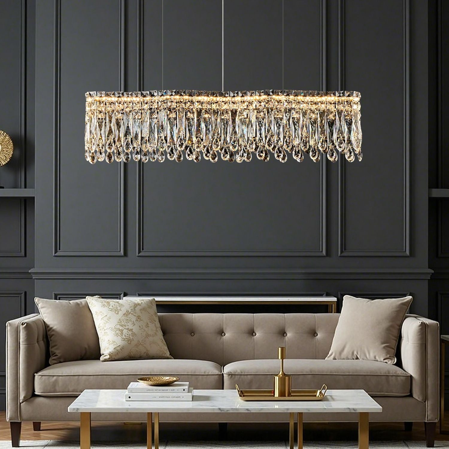 Flow Linear Modern Wave Integrated LED K9 Crystal Dining Chandelier in a living room — hanging above a beige sofa with decorative pillows, a marble coffee table, and a dark paneled wall backdrop | Sofary Lighting