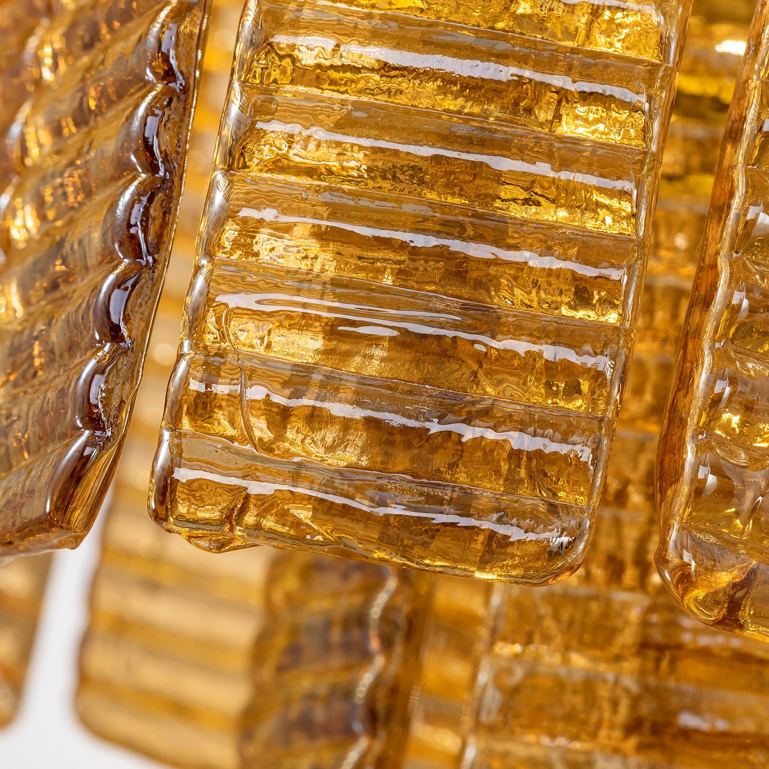 Close-up of ribbed amber glass chandelier panels with a crystalline, ice-like texture and warm honey tones. Sofary Lighting