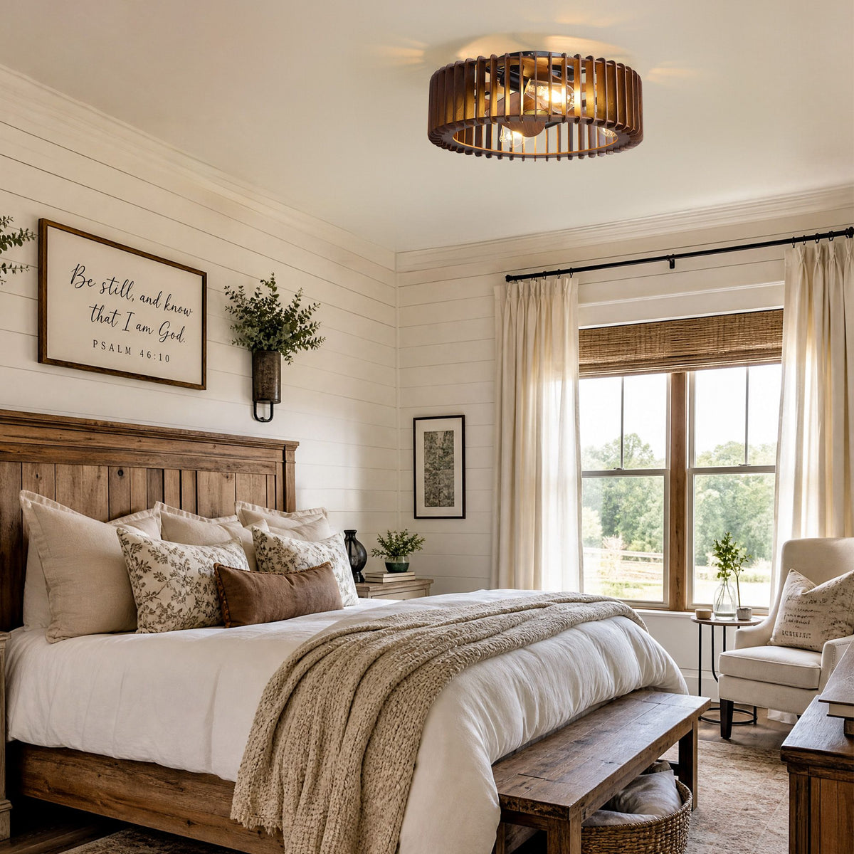 Industrial caged ceiling fan in farmhouse bedroom — dark wood bed, white bedding, decorative throw pillows, "Be still" wall art, large window with bamboo blinds and green views | Sofary Lighting