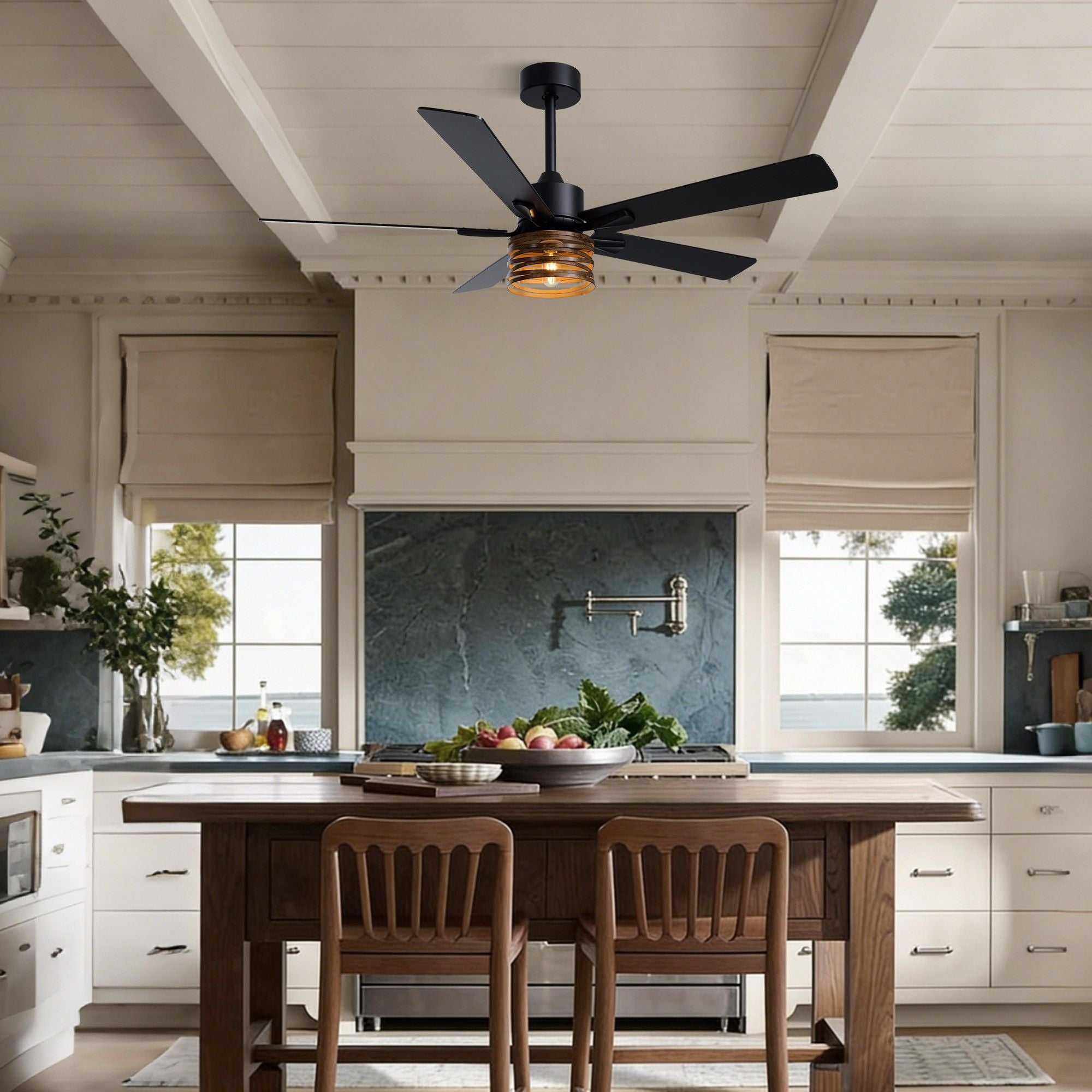 Industrial farmhouse ceiling fan over kitchen island — white cabinets, dark countertop, wood stools, windows with garden view, fruit bowl on counter | Sofary Lighting