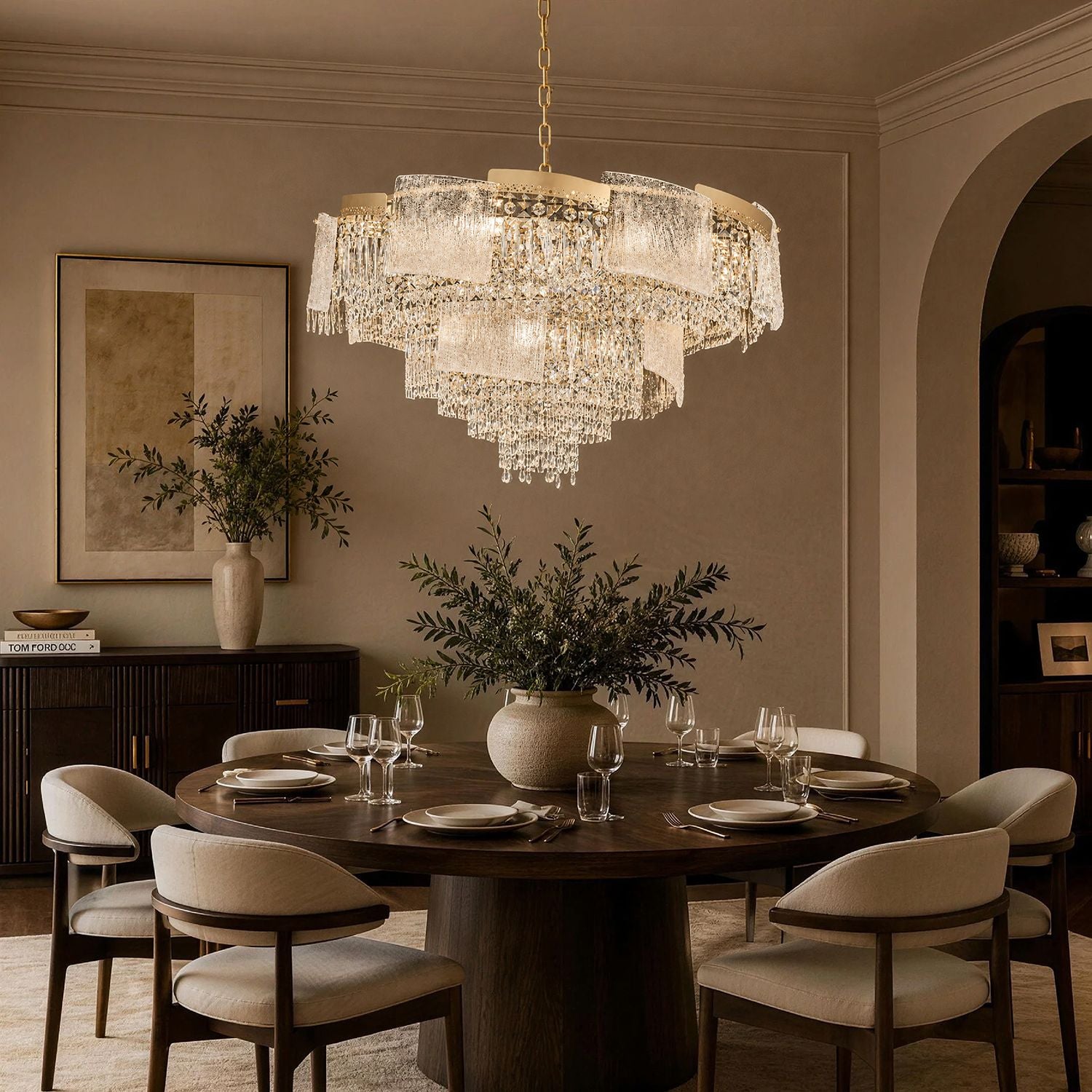 Aeria Crystal Chandelier illuminating a modern dining room — dark wood table, beige upholstered chairs, floral centerpiece, warm golden glow for dinner parties