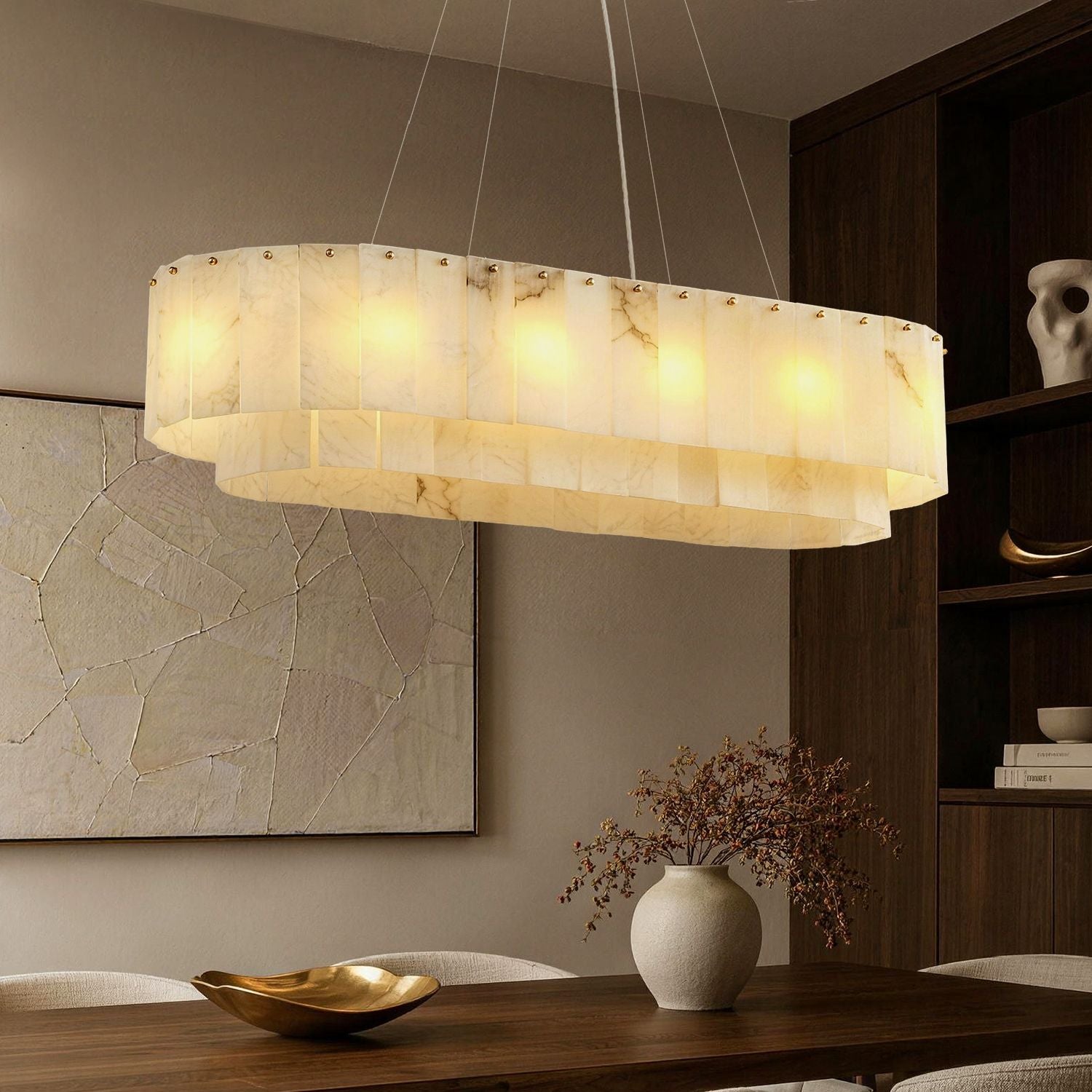 Aethel Modern Natural Alabaster Linear Chandelier in a dining room — featuring a tiered oval design with natural alabaster stone tiles, illuminated above a wooden dining table with elegant place settings and a dark wood cabinet in the background | Sofary Lighting