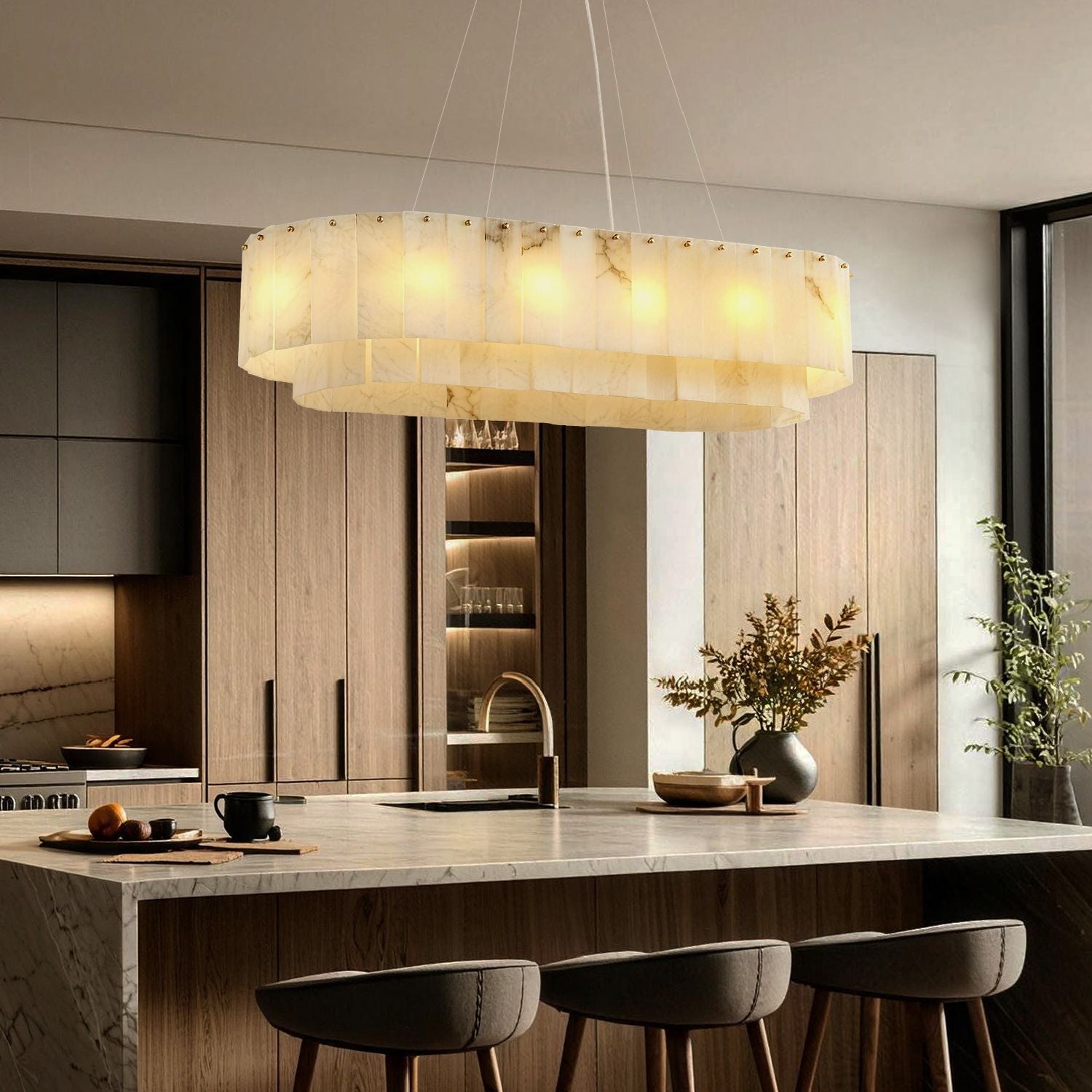 Aethel Modern Natural Alabaster Linear Chandelier in a modern kitchen — hanging above a marble kitchen island with wooden bar stools, pendant lights illuminating the workspace with cabinets and appliances in the background | Sofary Lighting