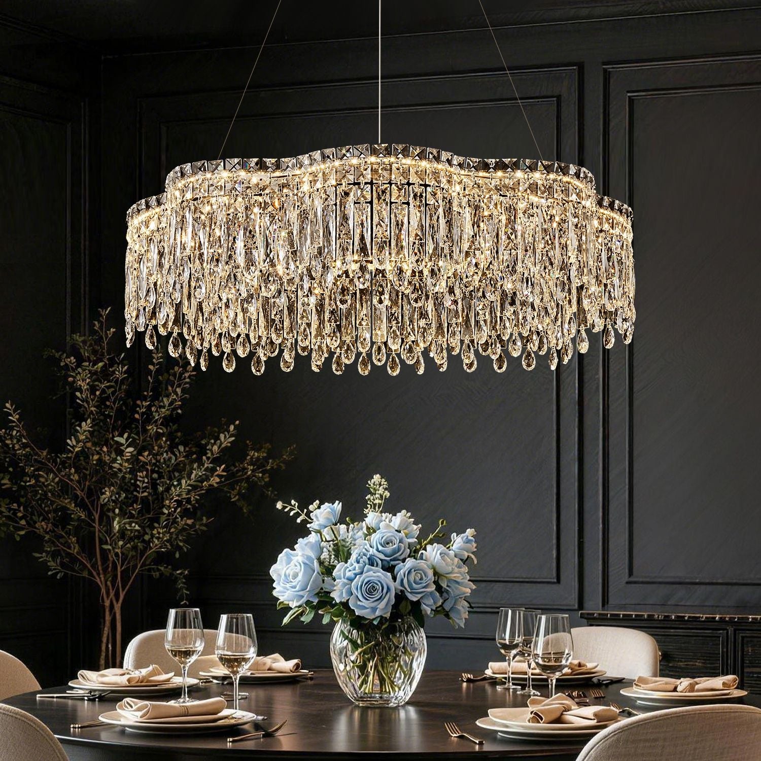 Luna Modern Wave Integrated LED K9 Crystal Ring Chandelier in a dining room — hanging above a dark wooden table with blue and white flowers, elegant tableware, and a black paneled wall backdrop | Sofary Lighting