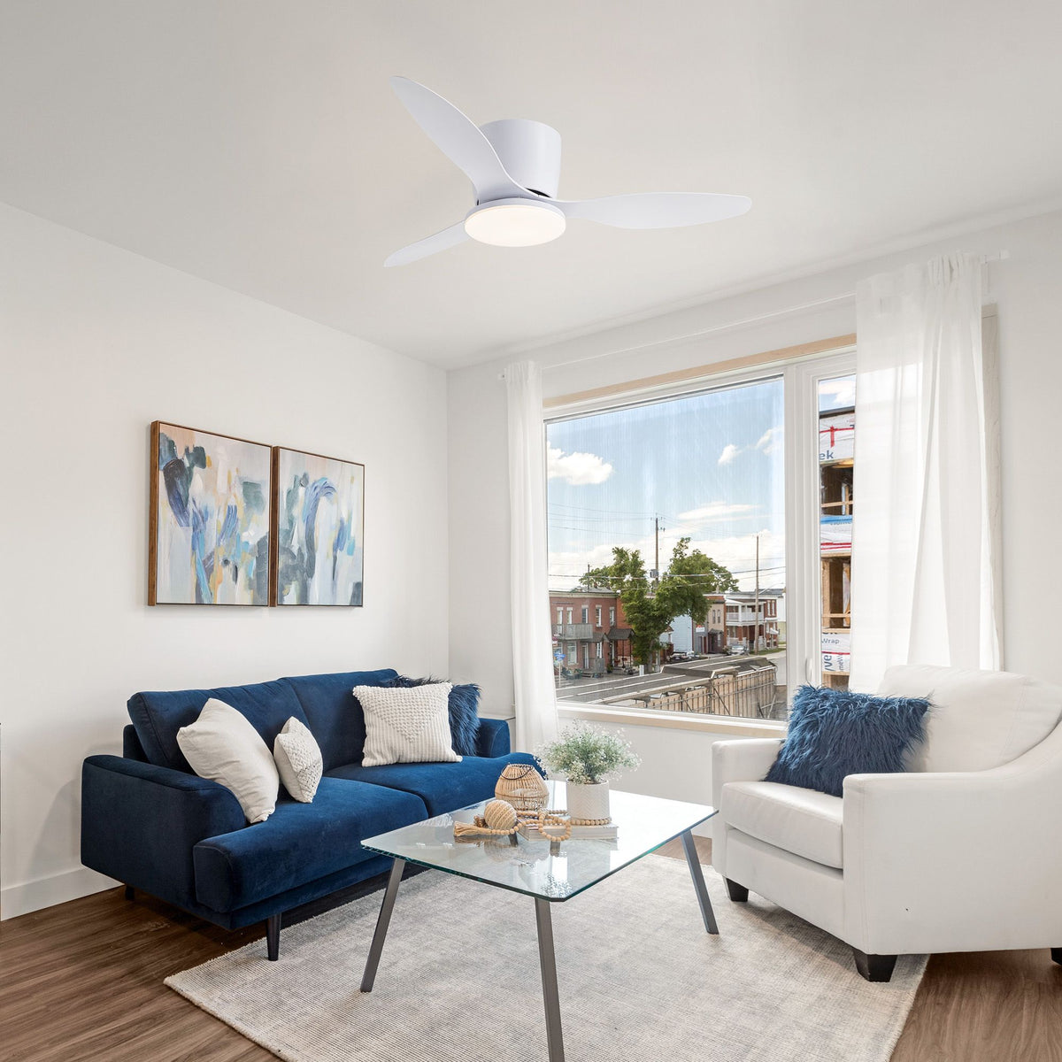 Modern white ceiling fan in living room — blue sofa, white armchair, glass coffee table, bright window view, minimalist home decor | Sofary Lighting