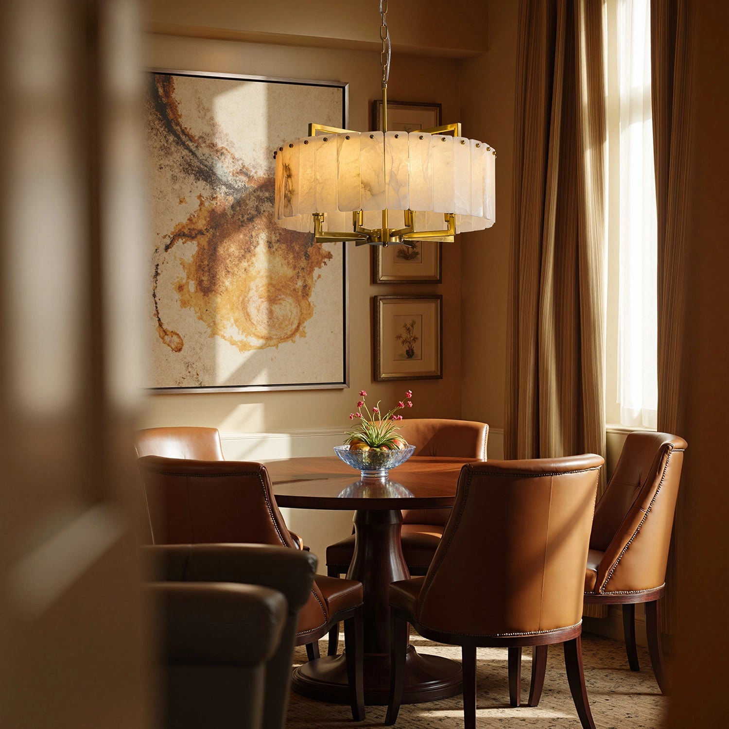 Round alabaster stone chandelier with brass accents hanging in a cozy dining nook with leather chairs and abstract wall art. Sofary Lighting