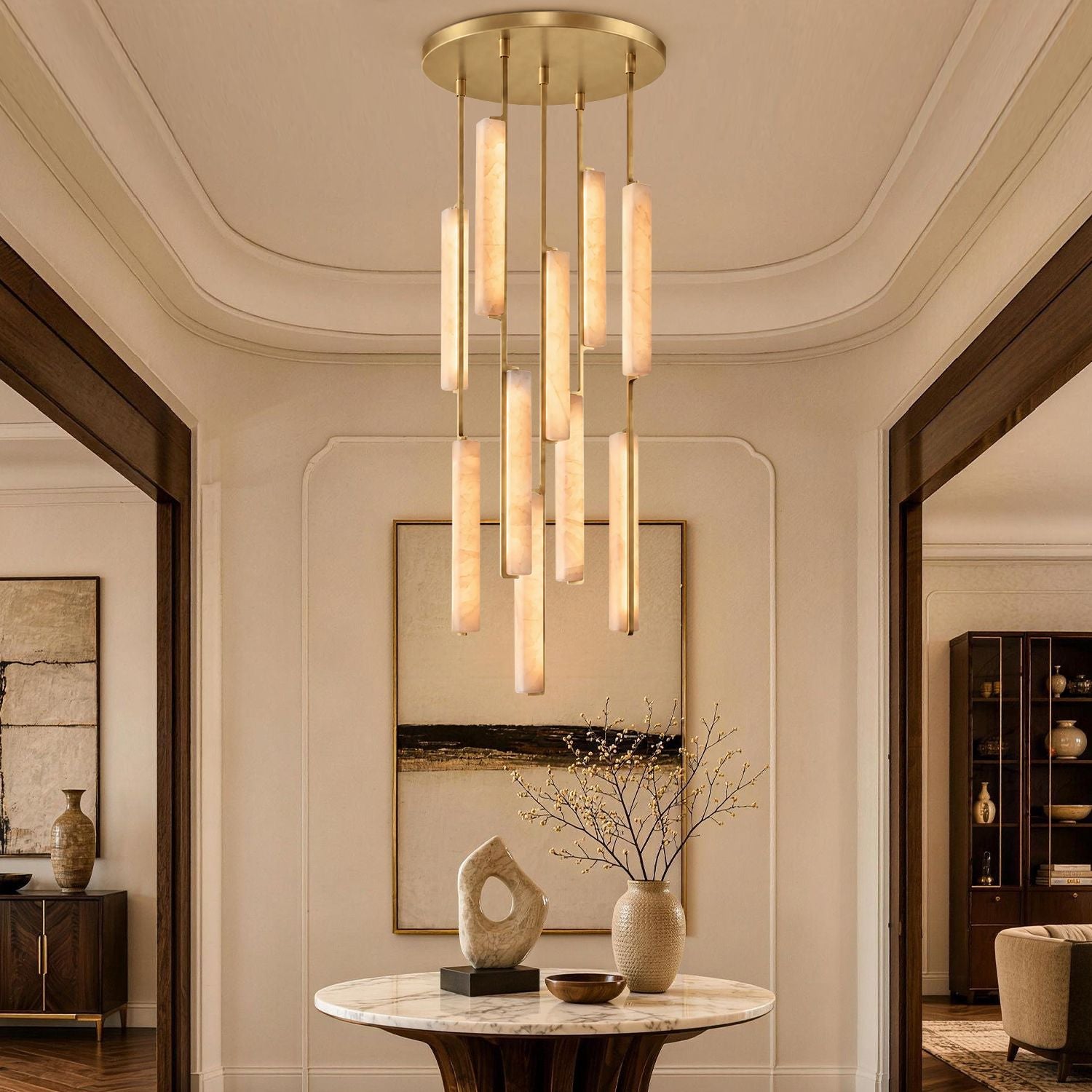 Stamen Modern Minimalist Alabaster Vertical Chandelier in a living room — hanging above a beige sectional sofa with abstract art and elegant decor, showcasing vertical alabaster rods with gold accents